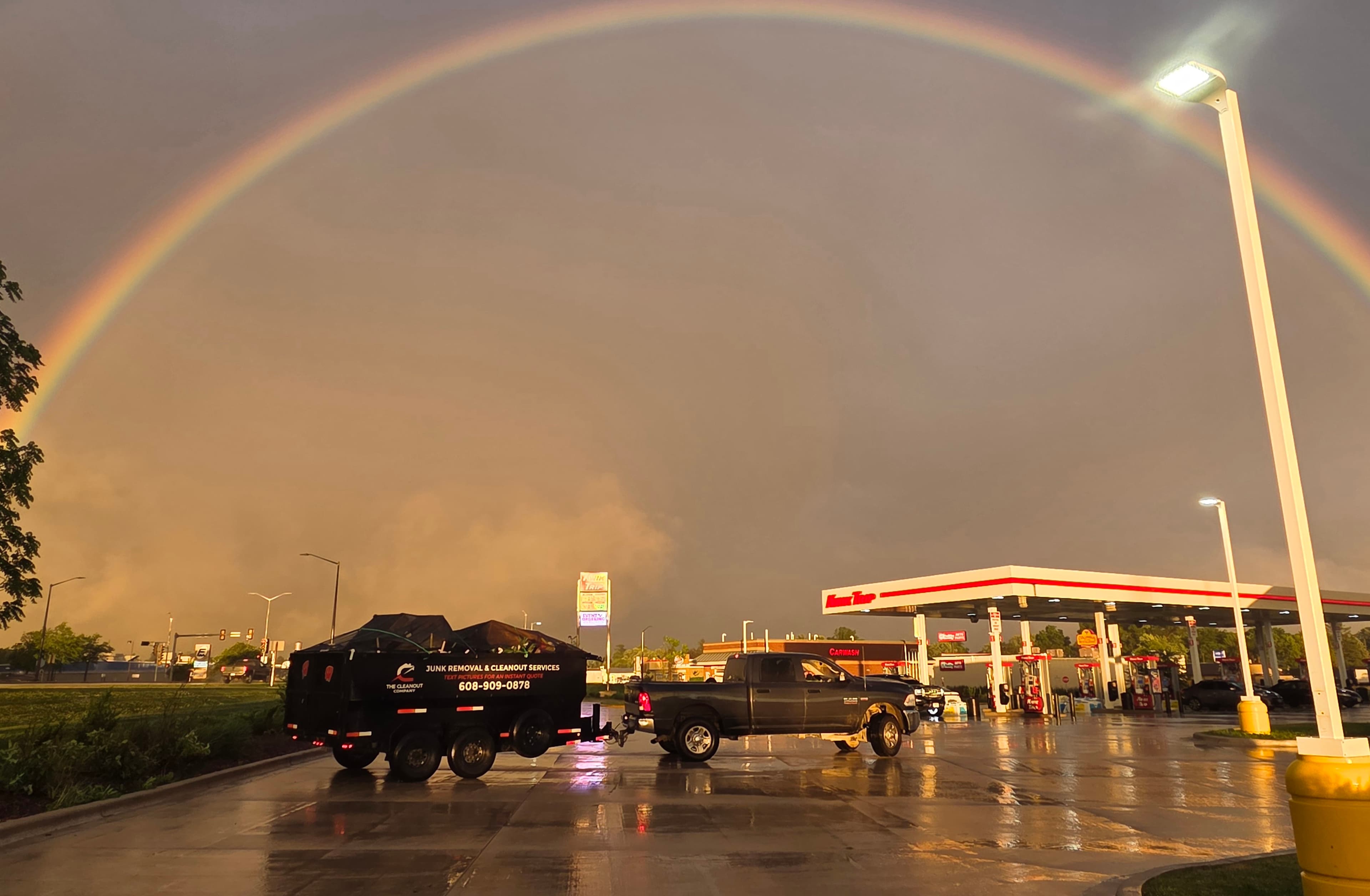 The Cleanout Company truck and loaded trailer under a full rainbow after a storm