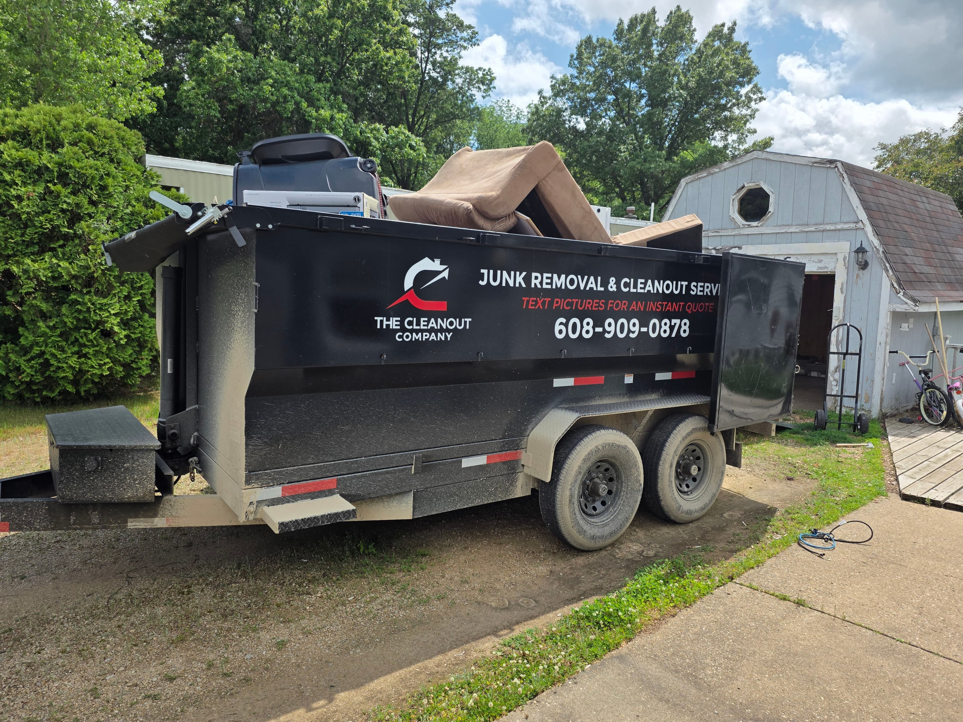 Cleanout Company trailer overfilled with a couch, recliner, and bin stacked above the top rail